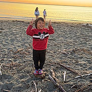 Ollie joined the competition — help win amazing prizes! child, beach, sunset, sand, ocean, peace_sign, smile, rock, driftwood, twilight, shore, person, casual_clothing, nature, outdoor, fun, happy, footwear, water, scenic