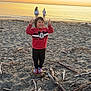 child, beach, sunset, sand, ocean, peace_sign, smile, rock, driftwood, twilight, shore, person, casual_clothing, nature, outdoor, fun, happy, footwear, water, scenic