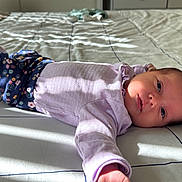 Lina Rose is registered to the contest to win money with this photo: baby, infant, bed, blanket, clothing, floral_pattern, purple, laying_down, portrait, face, hand, foot, sunlight, shadow, sleepwear, person, cute, indoors, resting, newborn