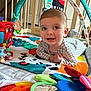 baby, infant, play_mat, toy, colorful, indoor, wooden_gate, smiling, happy, child, clothing, face, eyes, hand, floor, patterned, soft_toys, mirror, curious, crawling