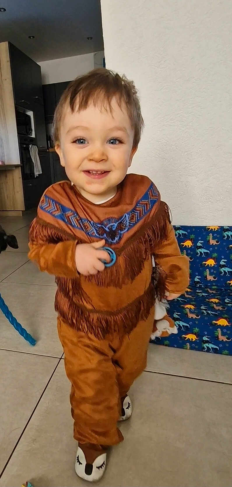 Aaron participe au concours pour gagner de l'argent avec cette photo : toddler, child, smiling, indoor, brown_outfit, fringes, blue_pattern, toy, slippers, dinosaur_print, floor_tiles, home, person, cute, happy, walking, young_child, playful, living_room, decor