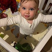 Tom participe au concours pour gagner de l'argent avec cette photo : baby, blue_eyes, child, clothing, cute, dinosaur, expression, face, floor_mat, hands, head, indoor, looking_up, onesie, person, play_area, playpen, plush, toddler, toy