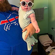 Brynlee is registered to the contest to win money with this photo: baby, child, sunglasses, beard, man, blue_hoodie, indoor, towel, clothing, person, holding, hand, face, portrait, furniture, cozy, casual, cute, fashion, funny