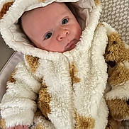 Maverick is registered to the contest to win money with this photo: baby, infant, face, eyes, clothing, hood, onesie, fur_texture, pattern, hand, couch, cushion, indoor, portrait, cute, warm, soft, child, newborn, cozy