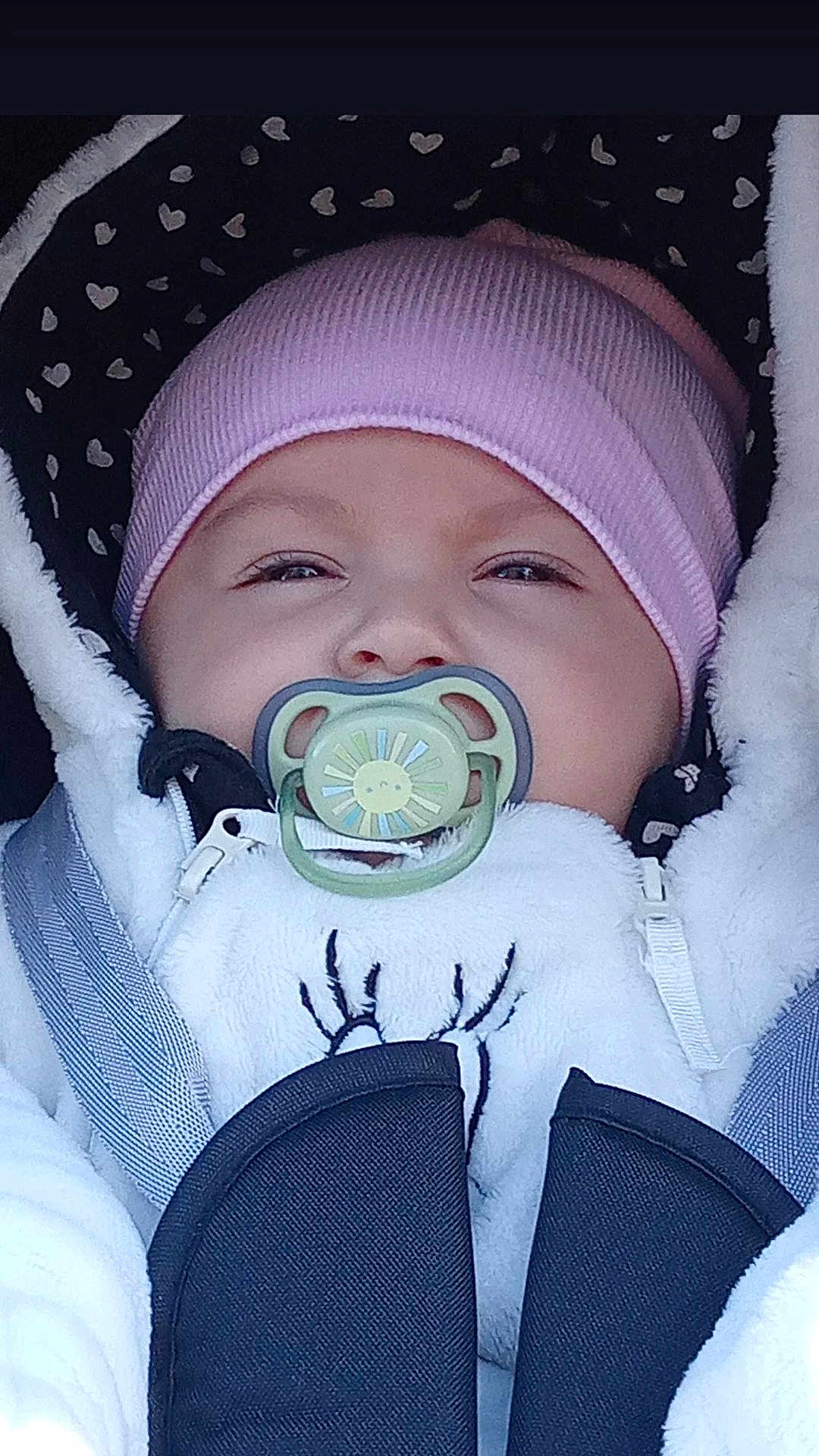 Leya participe au concours pour gagner de l'argent avec cette photo : baby, pacifier, beanie, white_jacket, car_seat, child, face, infant, cute, bundle, warm_clothing, pink, black, seatbelt, hooded_jacket, expression, portrait, closeup, winter_wear, sun_design