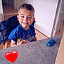 Érizio a rejoint le concours — aidez-le/la à gagner de superbes lots ! blue_shirt, boy, casual, child, door, furniture, happy, home, indoor, jacket, person, playful, red_heart_emoji, short_hair, sitting, smile, table, toy_car, toy_motorcycle, young_child