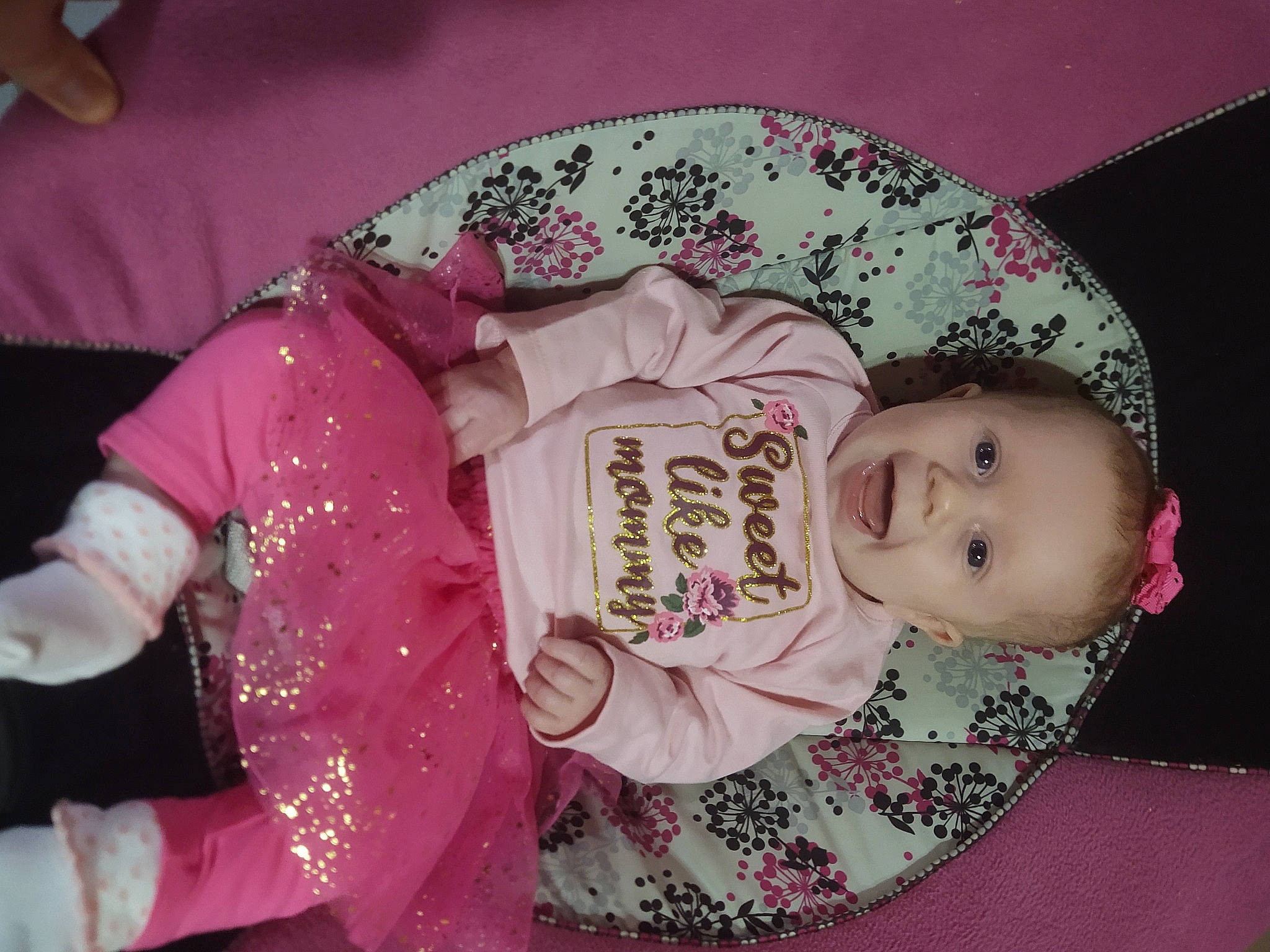 Nyla is registered to the contest to win money with this photo: baby, baby_products, baby_toddler_clothing, cheek, child, chin, embellishment, event, fashion_accessory, happy, head, human_body, magenta, pattern, person, pink, sitting, sleeve, smile, toddler