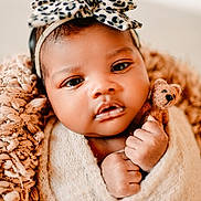 Abrianna is registered to the contest to win money with this photo: baby, infant, newborn, headband, bow, swaddle, blanket, plush_toy, teddy_bear, close_up, portrait, hands, eyes, cheeks, soft_texture, cozy, cute, dark_hair, studio_lighting, fabric
