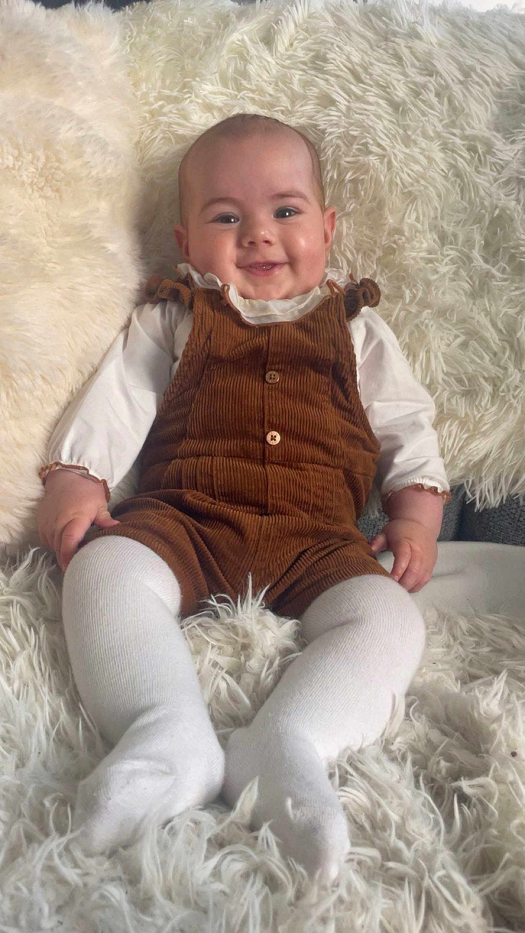 Victoria a rejoint le concours — aidez-le/la à gagner de superbes lots ! baby, infant, smiling, corduroy, overalls, white_tights, fluffy_rug, cozy, cute, child, portrait, indoor, happy, sitting, soft_texture, clothing, person, baby_girl, warm, relaxed