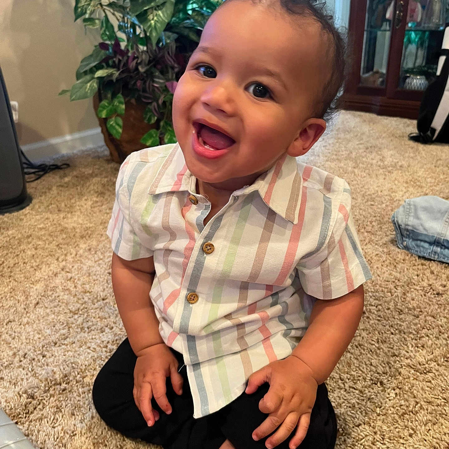 Zayden is registered to the contest to win money with this photo: barefoot, black_pants, cabinet, carpet, child, curly_hair, cute, door, furniture, happy, home, indoor, person, plant, portrait, sitting, smiling, striped_shirt, toddler, young_child