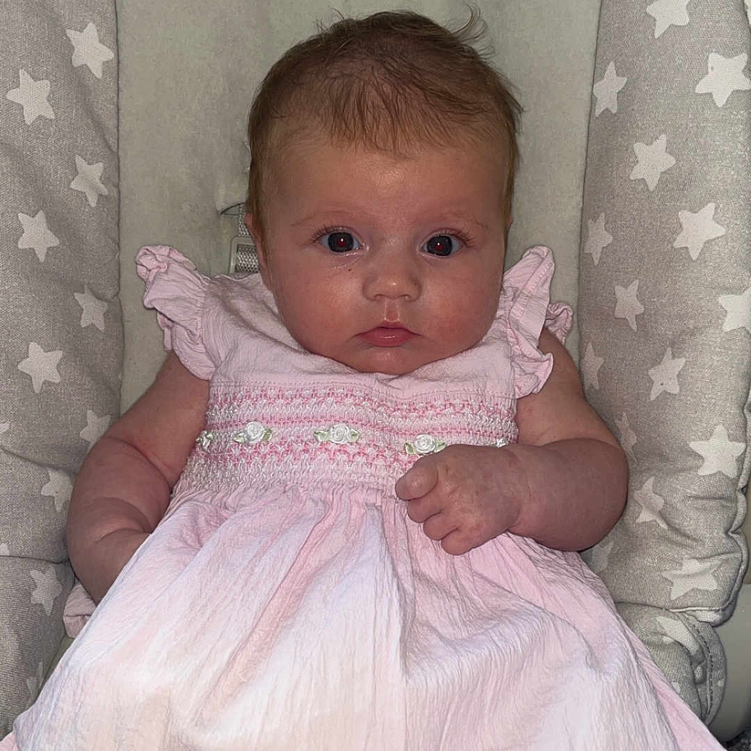 Marnie-Mai is registered to the contest to win money with this photo: baby, baby_chair, child, clothing, cushion, cute, eyes, face, hand, indoor, infant, looking_at_camera, person, pink_dress, portrait, seat_belt, sitting, skin, star_pattern, young_child