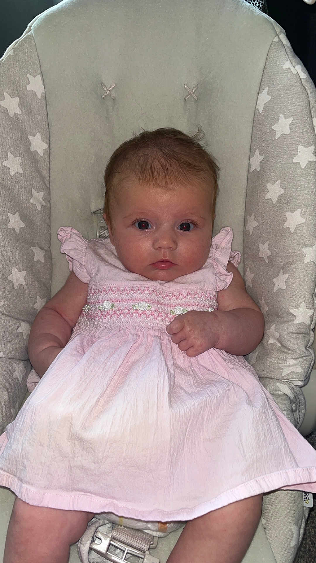 Marnie-Mai is registered to the contest to win money with this photo: baby, infant, child, pink_dress, baby_chair, star_pattern, face, eyes, hand, clothing, cushion, seat_belt, person, portrait, indoor, cute, young_child, sitting, looking_at_camera, skin