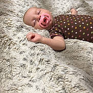 Evelyn is registered to the contest to win money with this photo: baby, bedroom, blanket, bottle, brown_onesie, child, colorful_dots, cozy, cute, furniture, home, indoors, infant, pacifier, peaceful, person, relaxing, sleeping, soft_texture, table