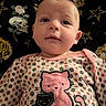 Evelyn joined the competition — help win amazing prizes! baby, blanket, cat_design, child, closeup, clothing, cute, face, floral_pattern, indoor, infant, looking_up, lying_down, onesie, patterned_clothing, person, portrait, rose_pattern, skull_pattern, stars
