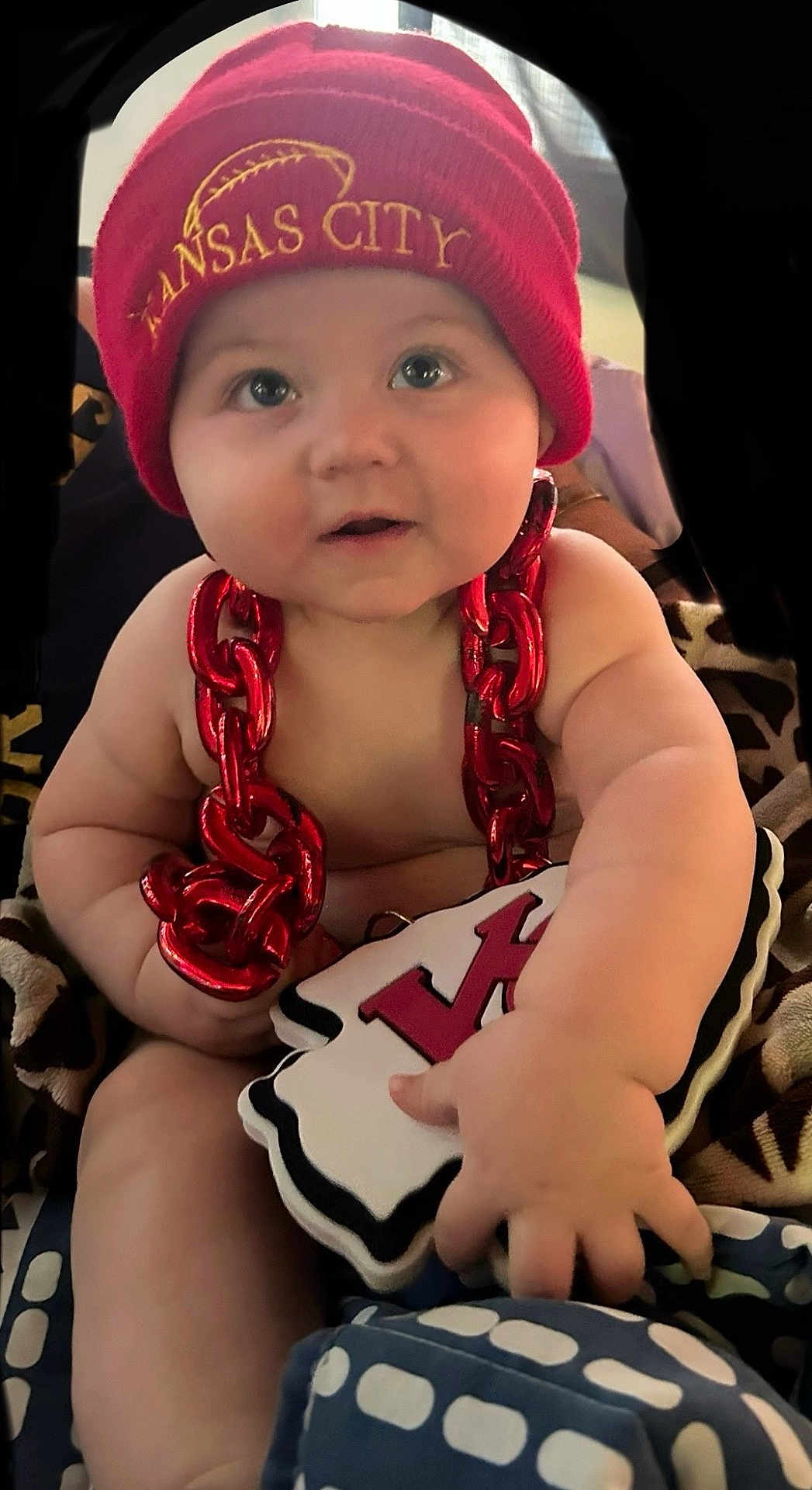 Timothy joined the competition — help win amazing prizes! baby, child, infant, red_hat, knit_cap, red_chain, plush_toy, hand, face, eyes, cheeks, skin, cute, indoor, blanket, pattern, soft_toy, football, sports_fan, smiling