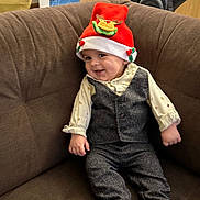 Mylhan participe au concours pour gagner de l'argent avec cette photo : baby, child, smiling, hat, red_hat, reindeer, vest, pants, couch, brown_couch, indoor, cute, festive, holiday, portrait, person, clothing, happy, sitting, infant