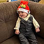 baby, child, smiling, hat, red_hat, reindeer, vest, pants, couch, brown_couch, indoor, cute, festive, holiday, portrait, person, clothing, happy, sitting, infant