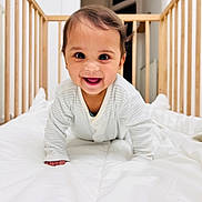 Arav joined the competition — help win amazing prizes! baby, infant, crib, crawling, smiling, happy, pajamas, wooden_crib, white_comforter, indoors, child, cute, face, portrait, bedroom, young_child, person, baby_clothes, playful, bright
