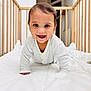 baby, infant, crib, crawling, smiling, happy, pajamas, wooden_crib, white_comforter, indoors, child, cute, face, portrait, bedroom, young_child, person, baby_clothes, playful, bright