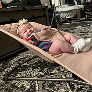 Josephine joined the competition — help win amazing prizes! baby, infant, smile, headband, baby_bouncer, socks, carpet, living_room, furniture, chair, table, person, child, happy, indoor, floor, cute, relaxing, clothing, home