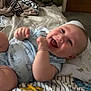 baby, infant, smiling, laughing, bed, blanket, patterned_sheet, clothing, indoor, furniture, happy, child, person, cute, cozy, soft_toys, room, relaxed, lying_down, skin