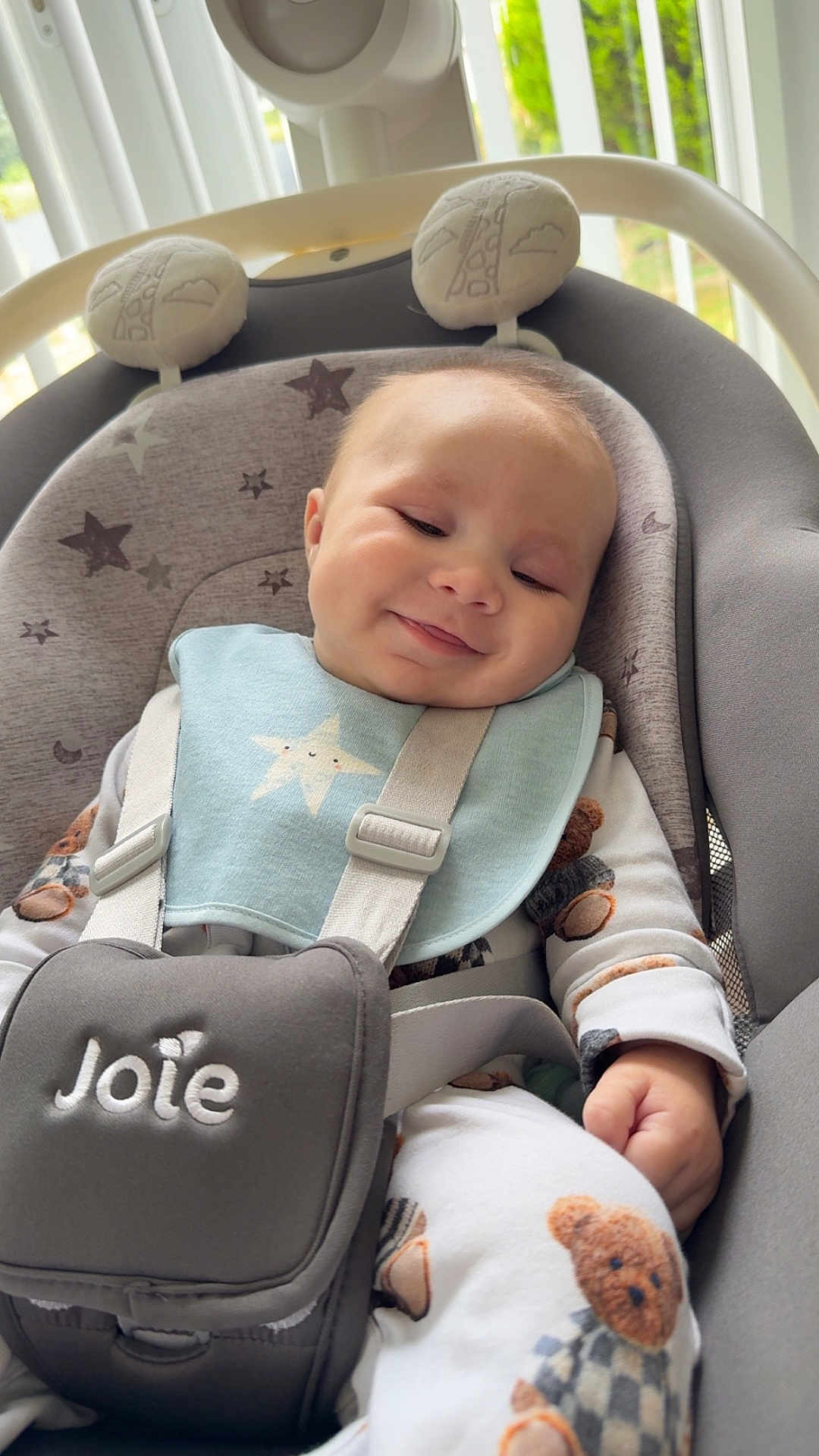George joined the competition — help win amazing prizes! baby, infant, smiling, baby_seat, car_seat, bib, pajamas, teddy_bear, soft_lighting, window_blinds, indoor, child, cute, happy, face, person, seatbelt, fabric, comfort, cozy