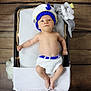 baby, infant, basket, knit_clothing, knit_hat, plush_toy, elephant_toy, blanket, wooden_floor, lying_down, cute, child, indoors, soft_toys, white_blanket, blue_accent, handmade, small_baby, cozy, relaxed