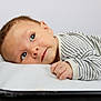 baby, infant, face, eyes, hand, blanket, striped_clothing, lying_down, basket, soft_texture, cute, curious, portrait, skin, head, newborn, indoors, resting, closeup, child