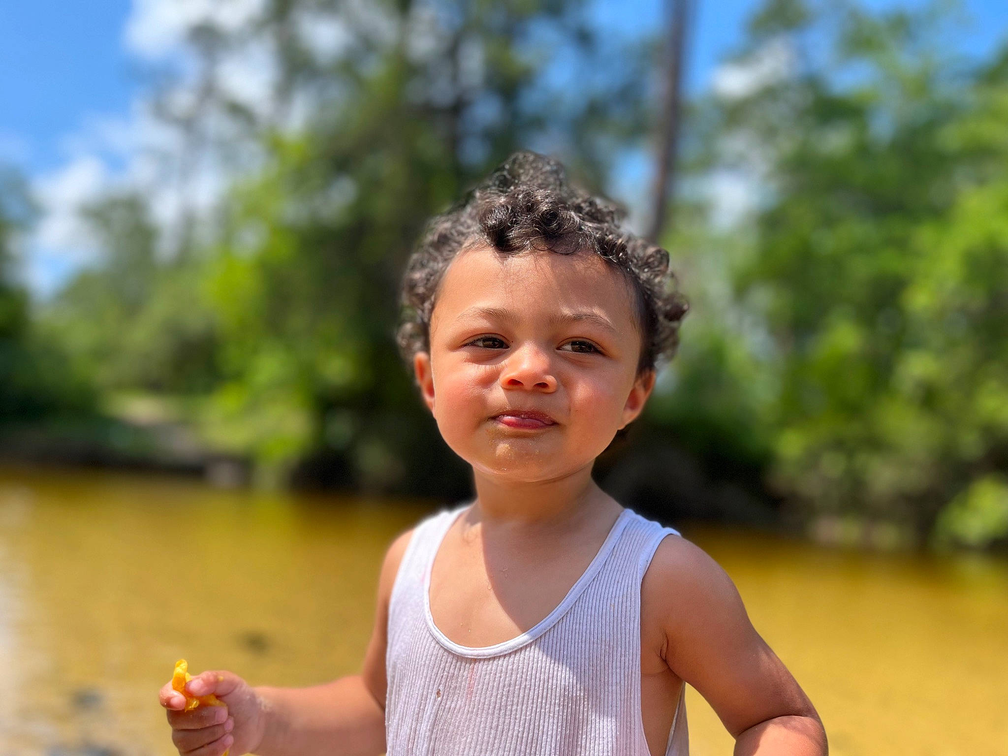 Kyree is registered to the contest to win money with this photo: body_of_water, child, eye, face, fun, grass, happy, lake, leisure, natural_environment, people_in_nature, person, recreation, sitting, sky, smile, toddler, travel, tree, vacation