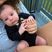 Stevie is registered to the contest to win money with this photo: baby, infant, person, hand, clothing, outdoor, porch, railing, grass, skin, face, holding, sitting, black_clothing, casual_wear, smile, closeup, human, tenderness, nature