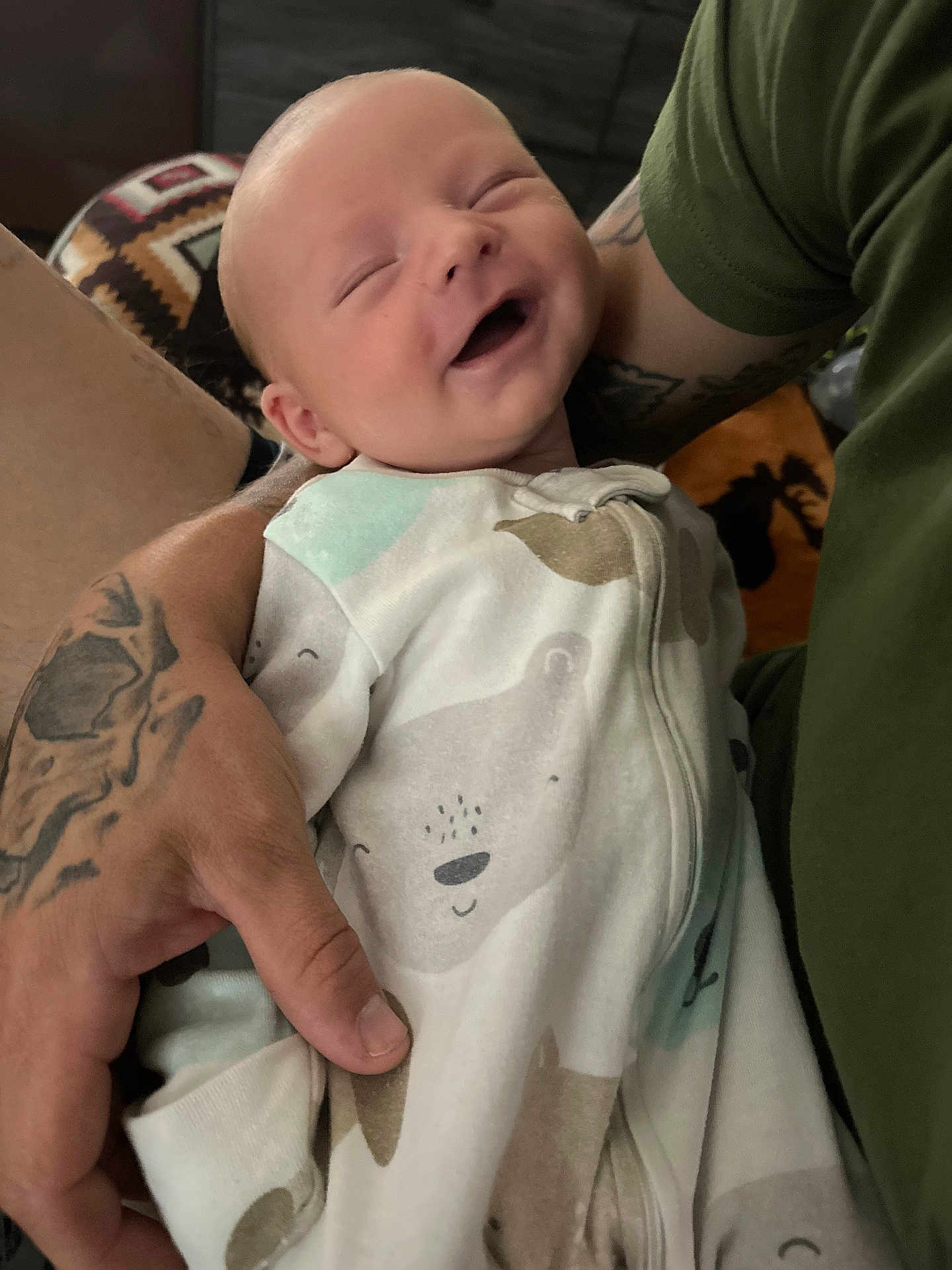 Maverick is registered to the contest to win money with this photo: baby, child, smiling, happy, person, infant, onesie, bear_print, tattoo, arm, hand, closeup, indoor, fabric, clothing, cute, sleepy, care, love, comfort