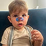 Noam participe au concours pour gagner de l'argent avec cette photo : baby, beige_shirt, blue_couch, bracelet, casual_clothing, child, closeup, curly_hair, cute, expression, face, hand, indoor, nose_bandage, person, portrait, sitting, suspenders, toddler, young_child