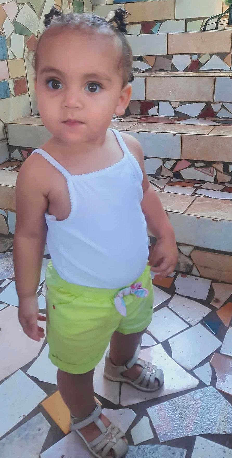Thaïss is registered to the contest to win money with this photo: casual_clothing, child, closeup, curious, curly_hair, daylight, innocent, lime_shorts, mosaic_floor, mosaic_stairs, outdoor, person, pigtails, portrait, sandals, standing, tile_pattern, toddler, white_tank_top, young_child