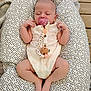 baby, sleeping, pacifier, onesie, heart_pattern, baby_lounger, cushion, wooden_deck, infant, cute, peaceful, relaxed, hands_up, legs_crossed, soft_fabric, pink, white, patterned, outdoor, resting