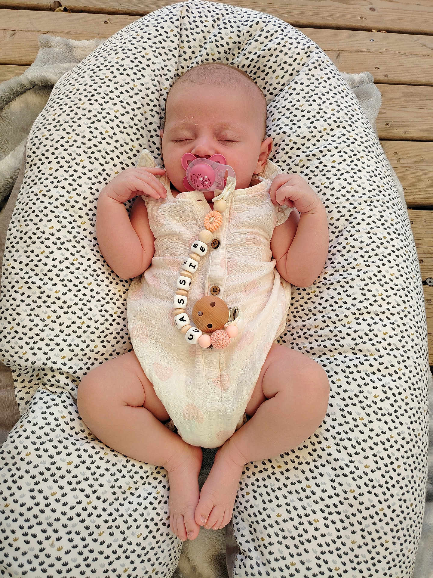 Cassie participe au concours pour gagner de l'argent avec cette photo : baby, sleeping, pacifier, onesie, heart_pattern, baby_lounger, cushion, wooden_deck, infant, cute, peaceful, relaxed, hands_up, legs_crossed, soft_fabric, pink, white, patterned, outdoor, resting