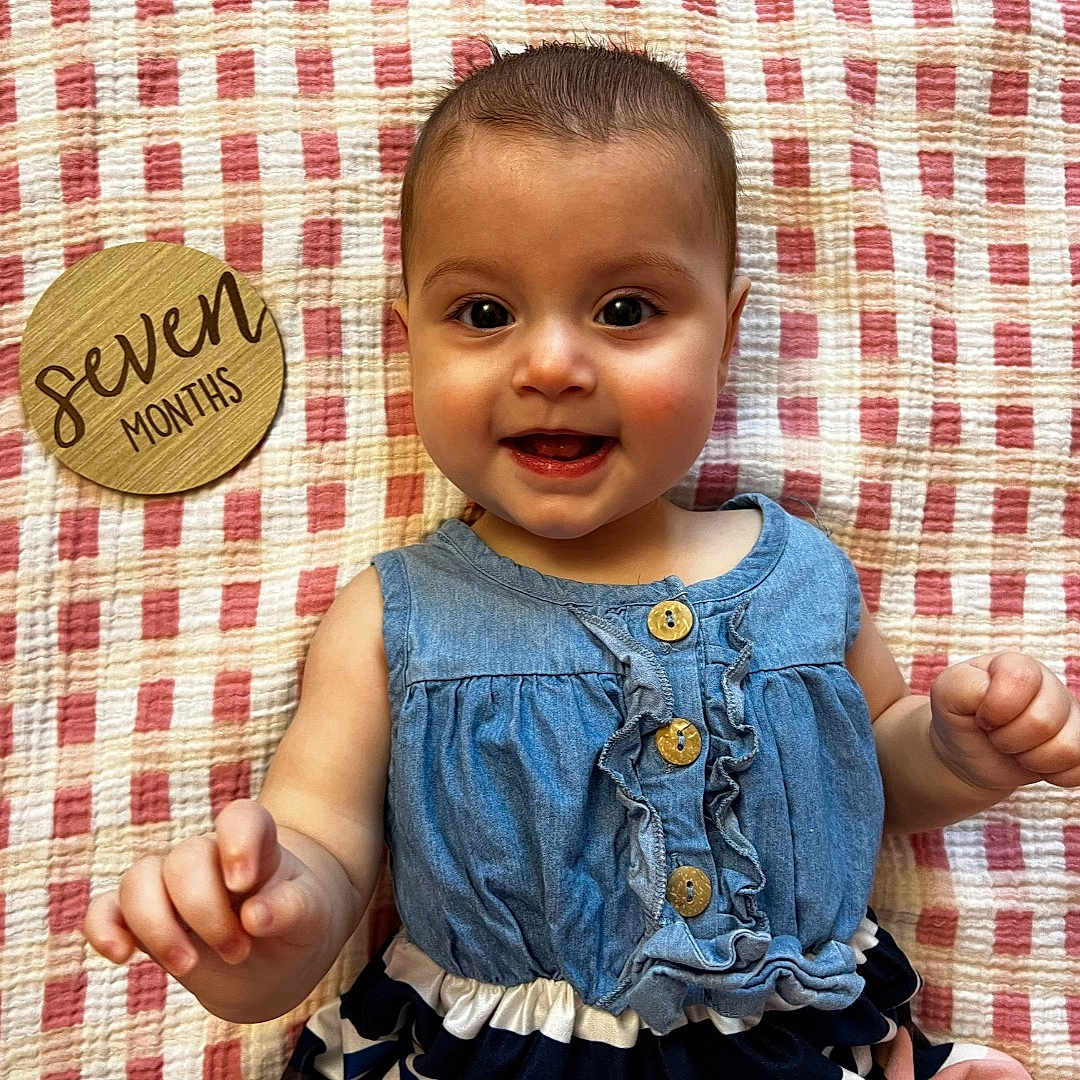 Lylah is registered to the contest to win money with this photo: baby, blanket, blue_clothing, buttons, checkered_pattern, child, cute, eyes, face, hands, happy, infant, lying_down, months, pink, portrait, ruffles, skin, smile, white