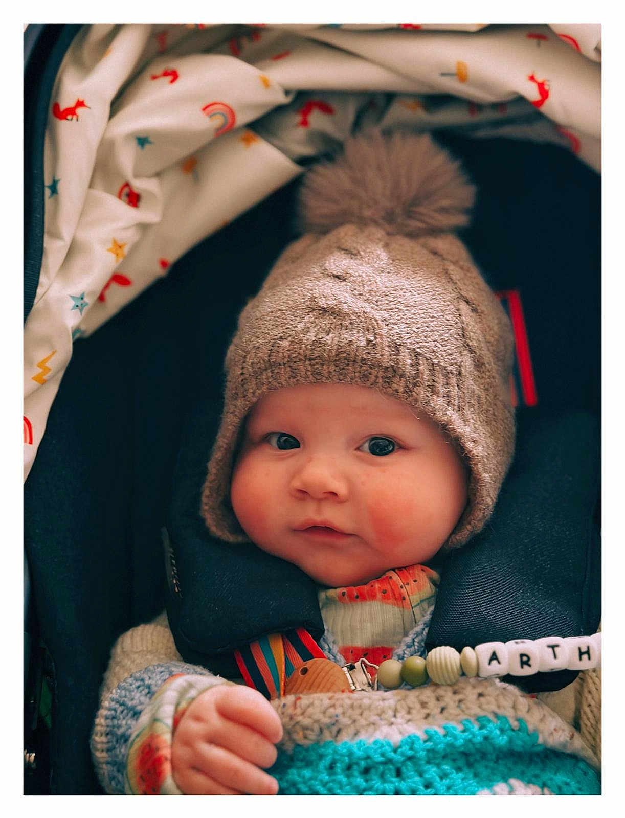 Arthur joined the competition — help win amazing prizes! baby, child, knitted_hat, pom_pom, blanket, colorful, pacifier_clip, face, chubby_cheeks, curious_expression, cozy, warm_clothing, indoor, portrait, infant, cute, soft_lighting, close_up, seated, person
