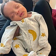 Jacyeon is registered to the contest to win money with this photo: baby, clothing, cozy, cute, furniture, hand, indoor, infant, lap, legs, living_room, moon, newborn, onesie, peaceful, person, portrait, sleeping, soft, stars