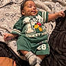 baby, infant, mickey_mouse, green_clothing, blanket, soft_texture, stars_pattern, socks, lying_down, hand, cute, smiling, dimples, child, indoor, portrait, cozy, clothing, person, comfortable