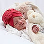 baby, child, clothing, cozy, cute, face, flower, hand, indoors, infant, newborn, peaceful, plush_toy, portrait, red_hat, resting, sleeping, soft_texture, teddy_bear, white_background