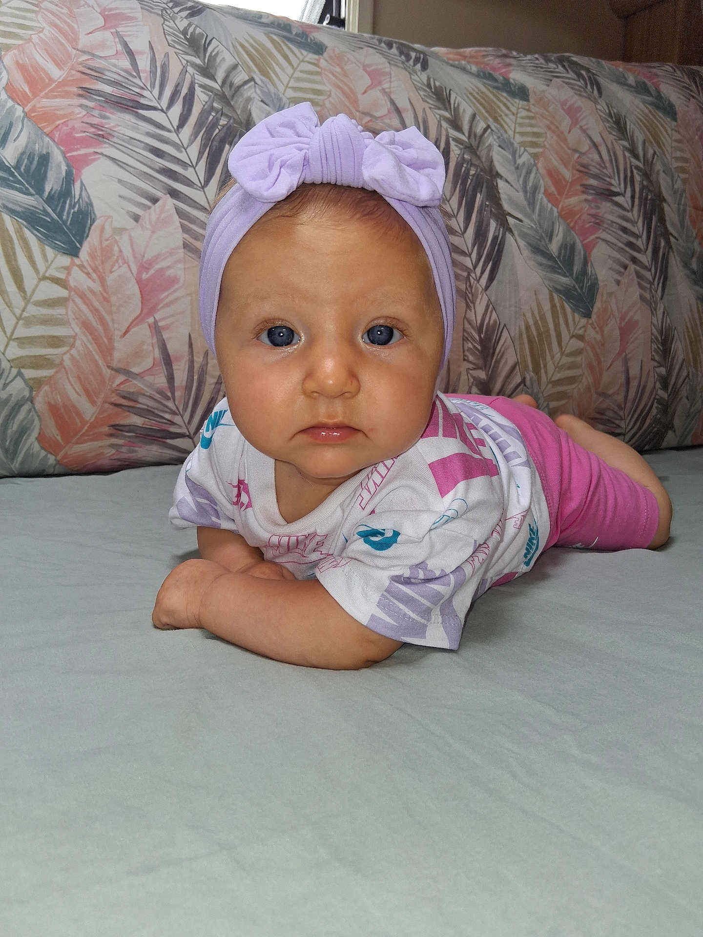 Shelsy a rejoint le concours — aidez-le/la à gagner de superbes lots ! baby, bed, blue_eyes, child, clothing, cute, face, hands, headband, indoor, infant, looking, lying_down, patterned_pillow, pillow, pink_shorts, portrait, skin, tummy, white_shirt