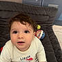 baby, child, curly_hair, cushion, cute, expression, eyes, face, hand, indoors, long_sleeve_shirt, looking_up, mouth, sitting, skin, soft_furniture, striped_pants, toddler, toy_ball, toy_ring