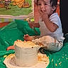 Ayden is registered to the contest to win money with this photo: toddler, cake, birthday, messy, smiling, indoor, plastic_sheet, white_clothing, frosting, toy, floor, celebration, party, child, person, food, playful, winnie_the_pooh, decor, happy