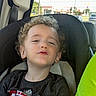 child, curly_hair, car_seat, tshirt, seatbelt, window, car_interior, boy, casual, relaxed, portrait, vehicle, daylight, seat, young_child, expression, clothing, sitting, person, indoors