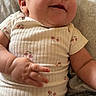 baby, infant, smiling, onesie, floral_pattern, chubby_cheeks, hand, face, skin, cute, happy, lying_down, soft_texture, clothing, casual, child, person, indoors, comfort, portrait