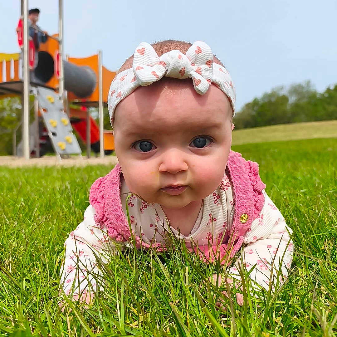 Emy a rejoint le concours — aidez-le/la à gagner de superbes lots ! baby, child, grass, headband, pink_clothing, outdoor, playground, slide, climbing_wall, person, greenery, summer, cute, infant, nature, park, young_child, face, portrait, daylight