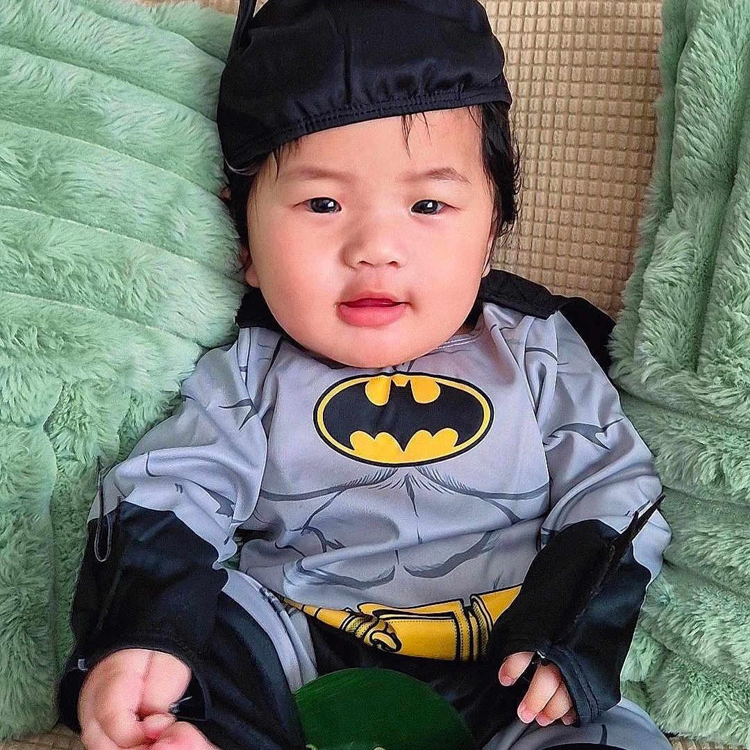 Ravine joined the competition — help win amazing prizes! baby, batman_costume, beige_couch, black_hat, child, costume, couch, cute, face, foot, green_pillow, hand, indoors, infant, portrait, sitting, smile, soft_texture, yellow_logo, young_child