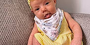 Leighton joined the competition — help win amazing prizes! baby, infant, child, yellow_dress, headband, tongue_out, sitting, couch, gray_fabric, textured_fabric, white_wall, playful, cute, indoors, portrait, bandana, floral_pattern, skin, legs, arms