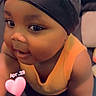arms, baby, black_cap, cap, child, closeup, cute, expression, eyes, face, headwear, indoor, infant, love_heart, person, portrait, skin, smiling, yellow_top, young_child