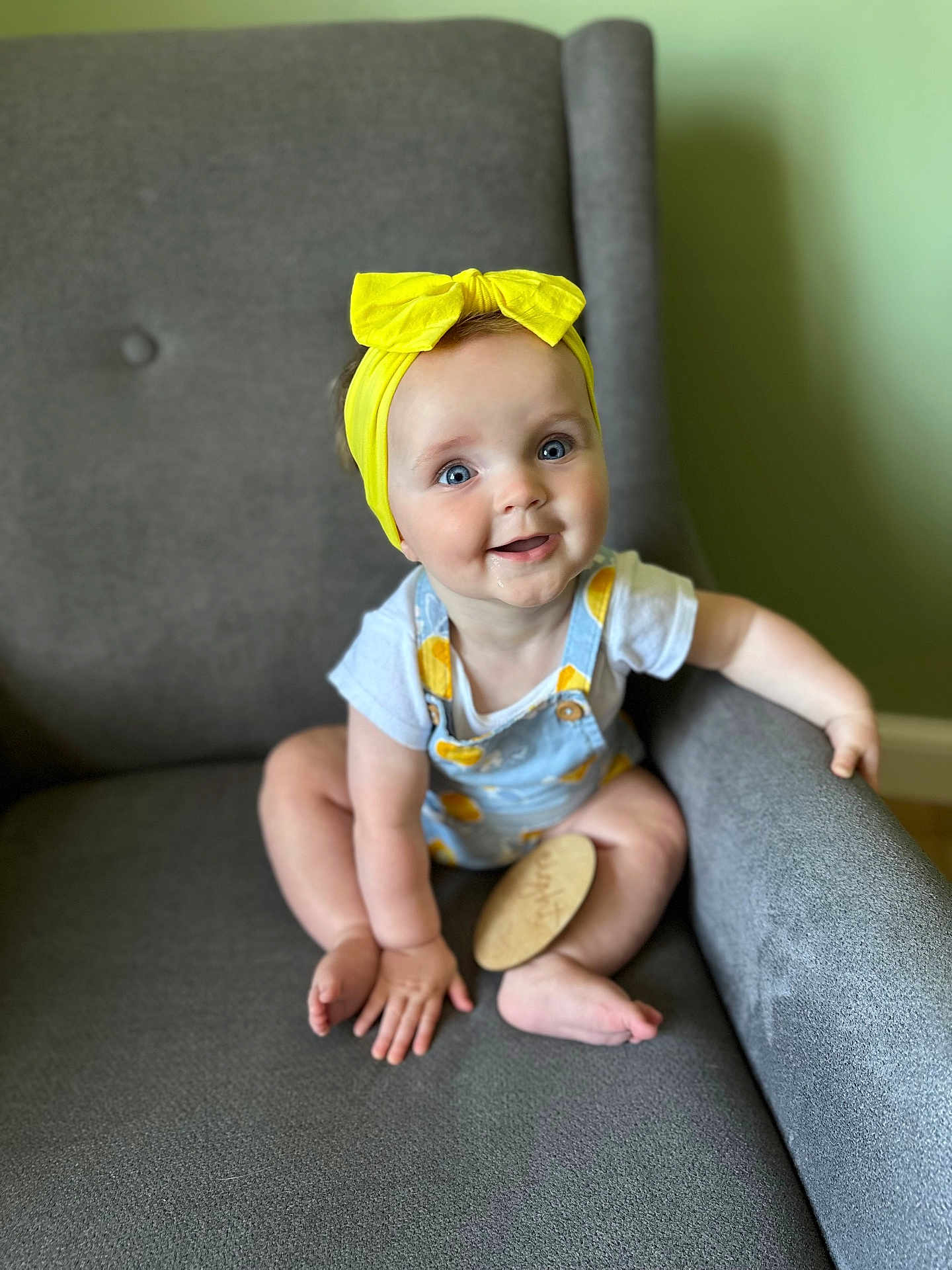 Wyatt joined the competition — help win amazing prizes! baby, child, infant, yellow_bow, headband, blue_eyes, smiling, drool, overalls, gray_armchair, sitting, happy, cute, indoor, person, short_sleeves, plush, skin, hand, foot